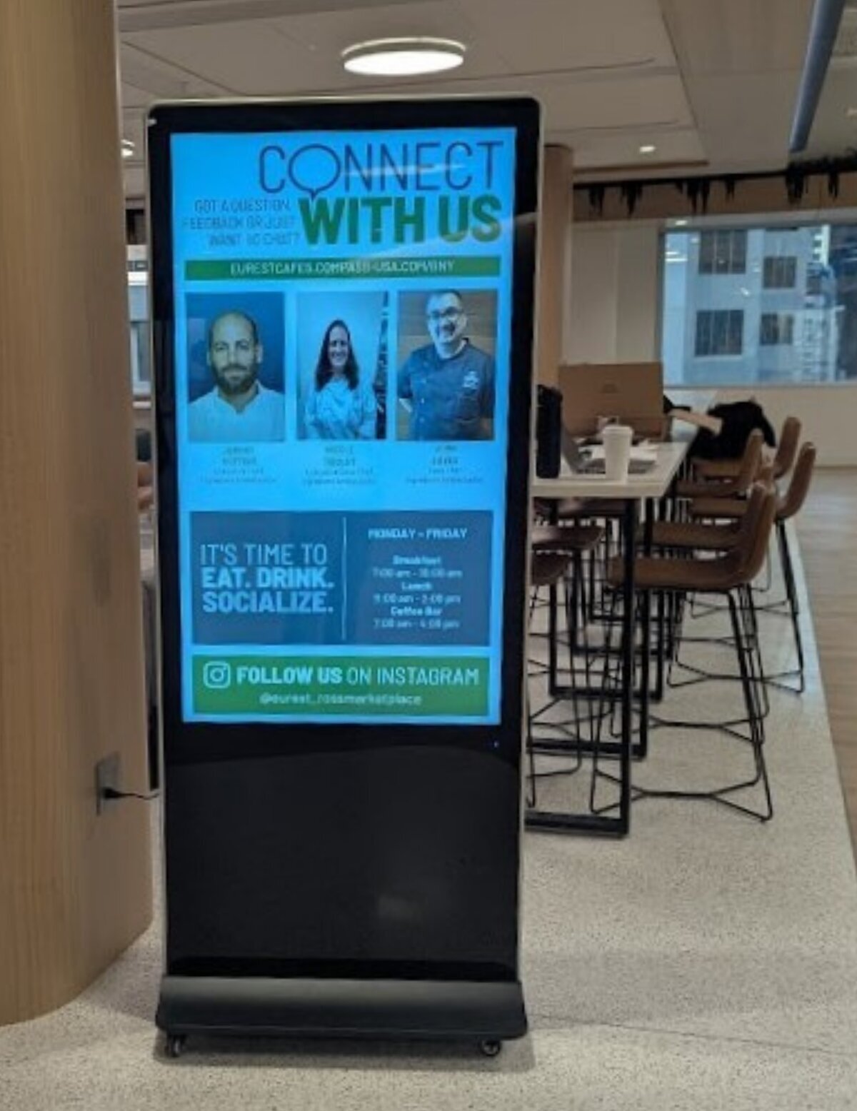 Freestanding digital poster kiosk on rollers showing a Connect With Us cafe screen in a dining area