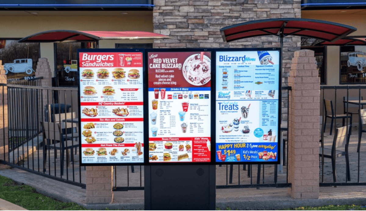 Three-screen outdoor digital menu board on a pedestal outside a fast food restaurant